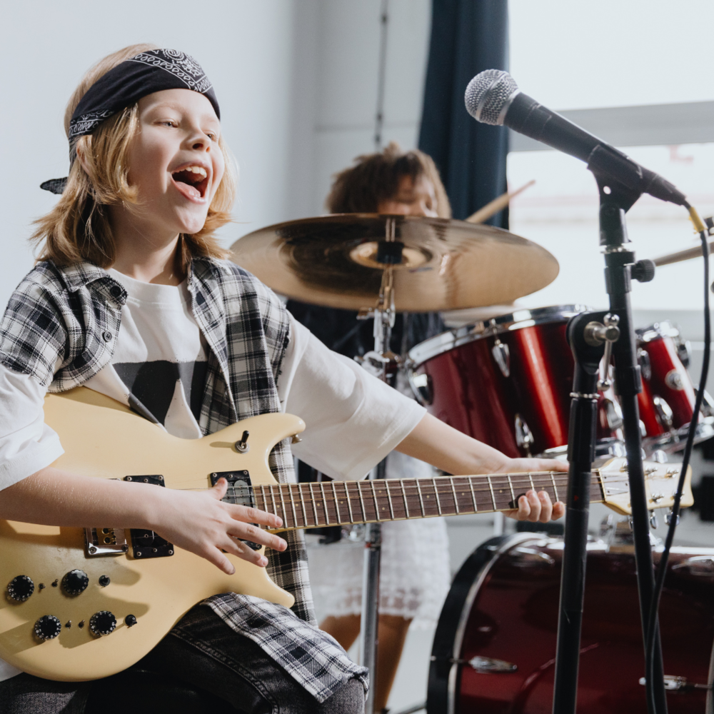 A student plays guitar, while another plays drums.