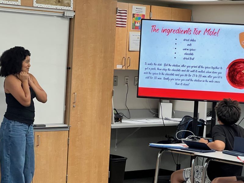 A student gives an oral presentation on food and culture. Un estudiante da una presentación oral sobre la comida y la cultura.