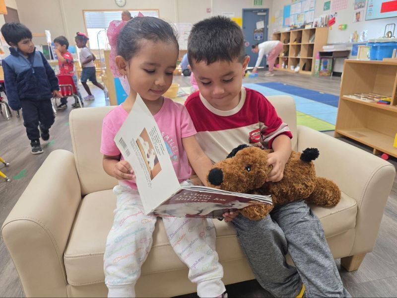 Preschool students  read a book on a mini couch.