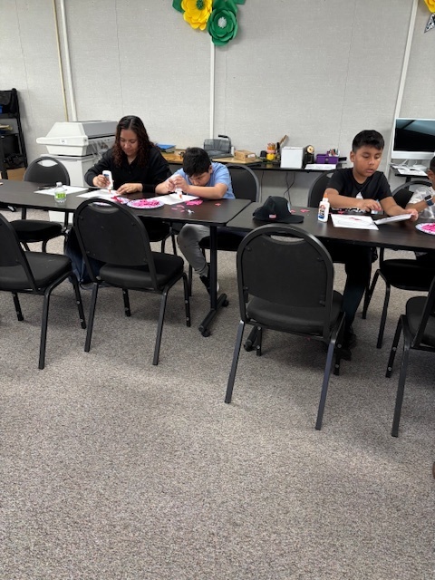 A mom and two students are sitting down while working on their heart collage projects.