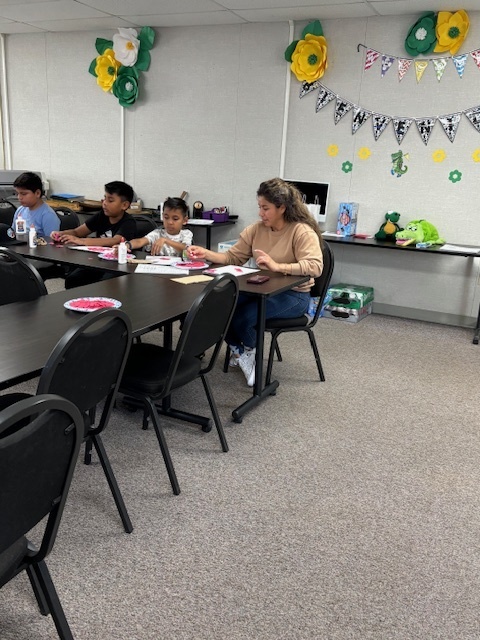 Mom Alma Villegas and her 3 children sit and work on a heart collage project.