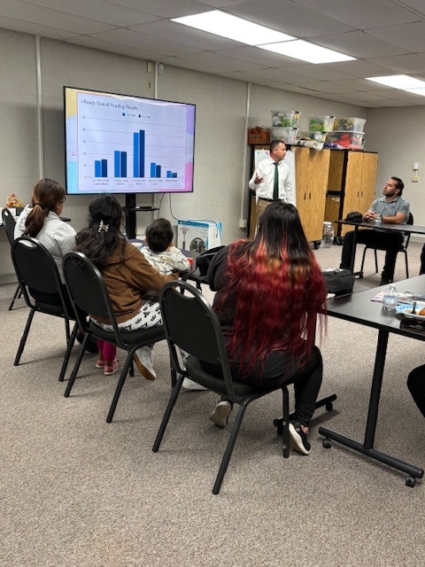Principal Lopez stands on the side of a smart TV and shares iReady data to parents attending Coffee with the Principal