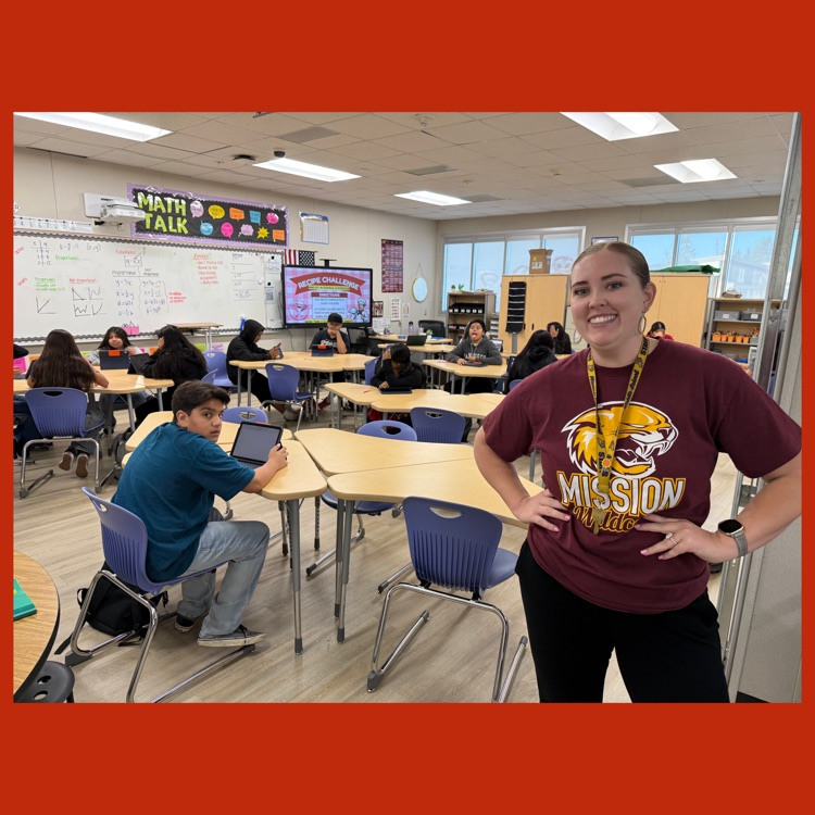 A photo of Ms. Kelly smiling for the camera as her 7th Grade students do the "Recipe Challenge" activity