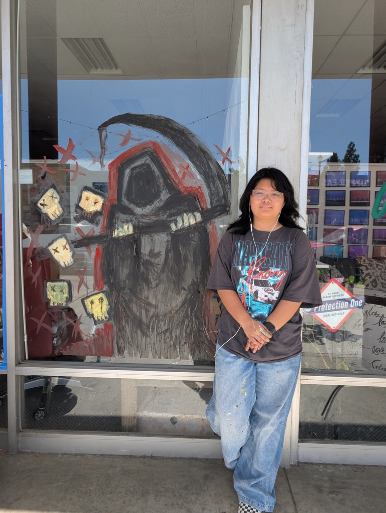 Sophia Ranion behind her Halloween window painting of a grim reaper.