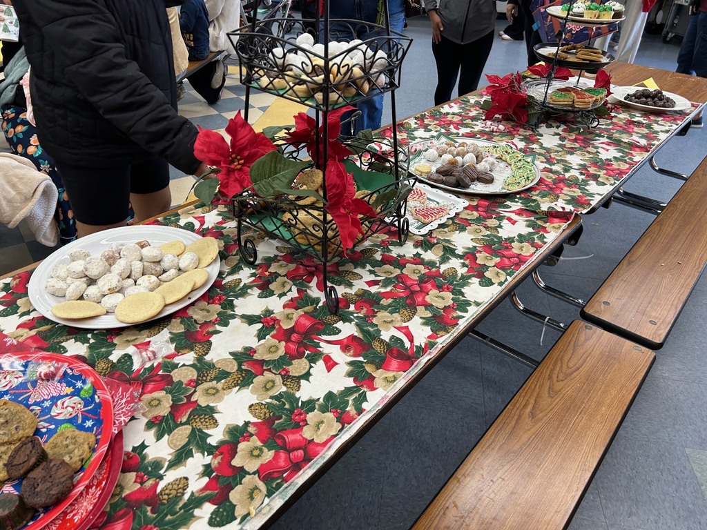 Festive table with a holiday-themed tablecloth, adorned with platters of assorted cookies. Decorative poinsettias enhance the seasonal atmosphere.