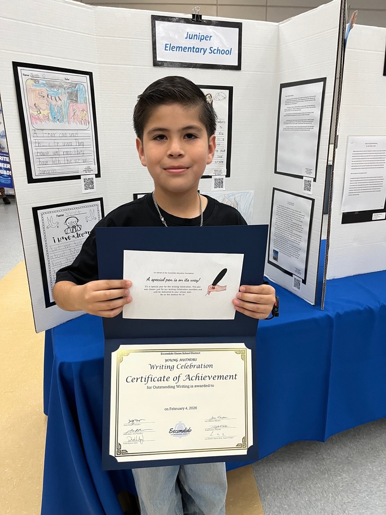 Student holding their award with their writing in the background