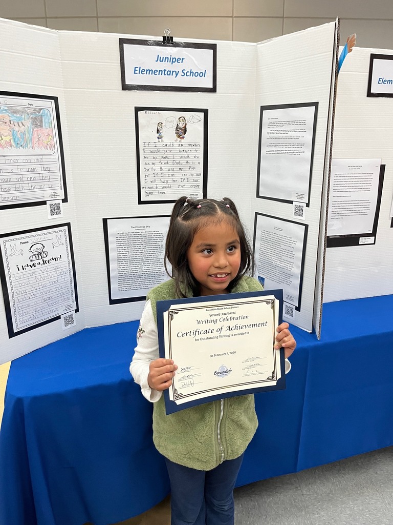 Student holding their award with their writing in the background