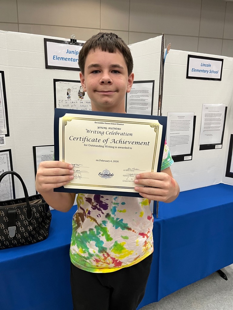 Student holding their award with their writing in the background