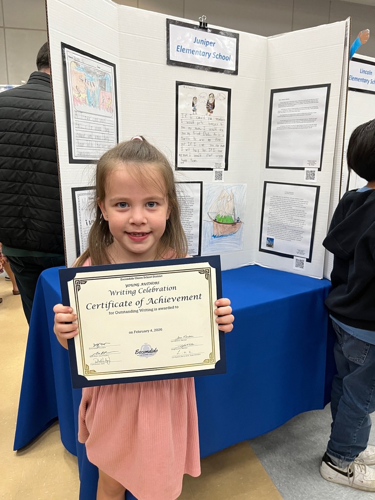 Student holding their award with their writing in the background