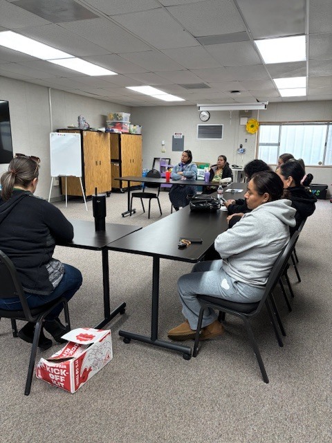 Seven moms are sitting on chairs in a u shaped desks and listen to what Principal Lopez is saying during Coffee with the Principal. 