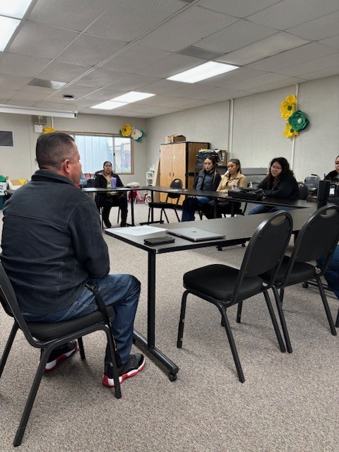 Principal Lopez is sitting on a chair inside room 21 and is talking to five parents during Coffee with the Principal 