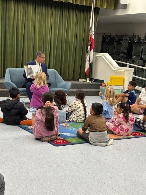 Superintendent Dr. Ibarra reads to 10 students inside the multipurpose room.