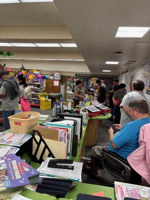 Five parents and one student are inside the library looking at the book fair along with Mrs. Preece the librarian and her husband.