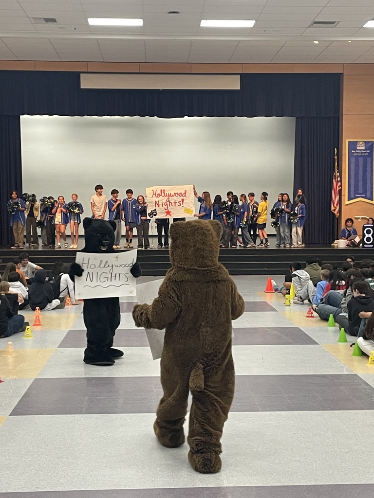 Students on stage holding signs and bear mascots in audience