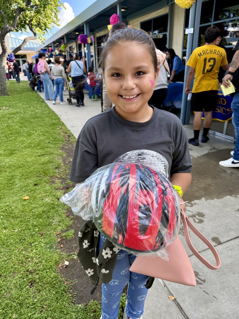  "A smiling young girl holds a packaged bicycle helmet she received at an outdoor school community event."