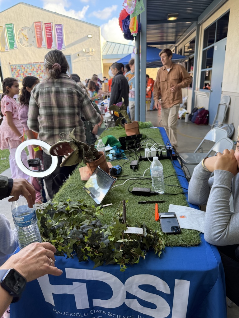  "A display table from the Halicioğlu Data Science Institute featuring carnivorous plants, electronics, and science materials at an outdoor community event."