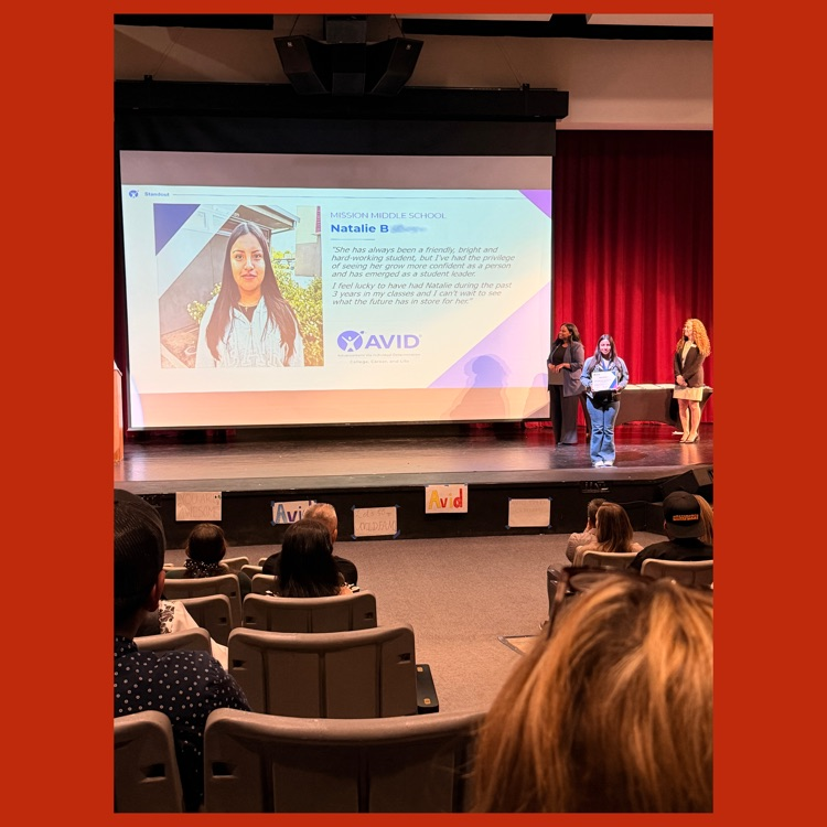 Natalie on stage receiving her recognition with a slide deck of her accomplishments on screen