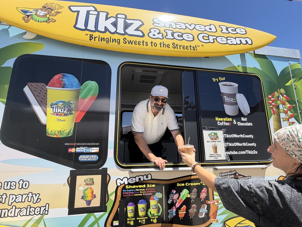 A vendor inside a Tikiz food truck hands an iced drink out the service window to a customer.