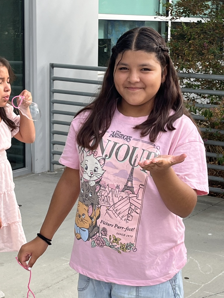Two students taking part in a hands-on lab activity to learn about cell membranes using common household items. One student is holding a bubble on the palm of her hand, the other is blowing a bubble. 