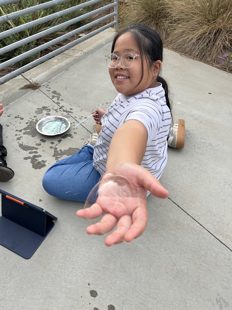 Student sitting on the ground. She is taking part in a hands-on lab activity on cell membranes through simple household items!