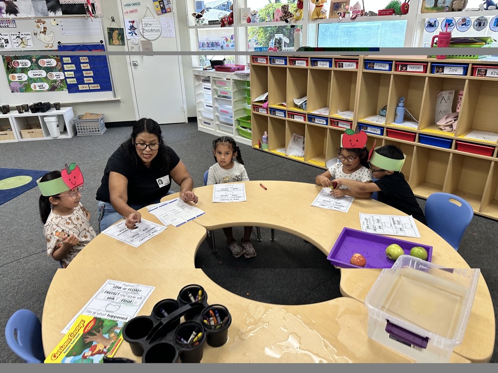 Children wearing apple crowns participate in an apple-themed classroom activity involving apple slices, worksheets.