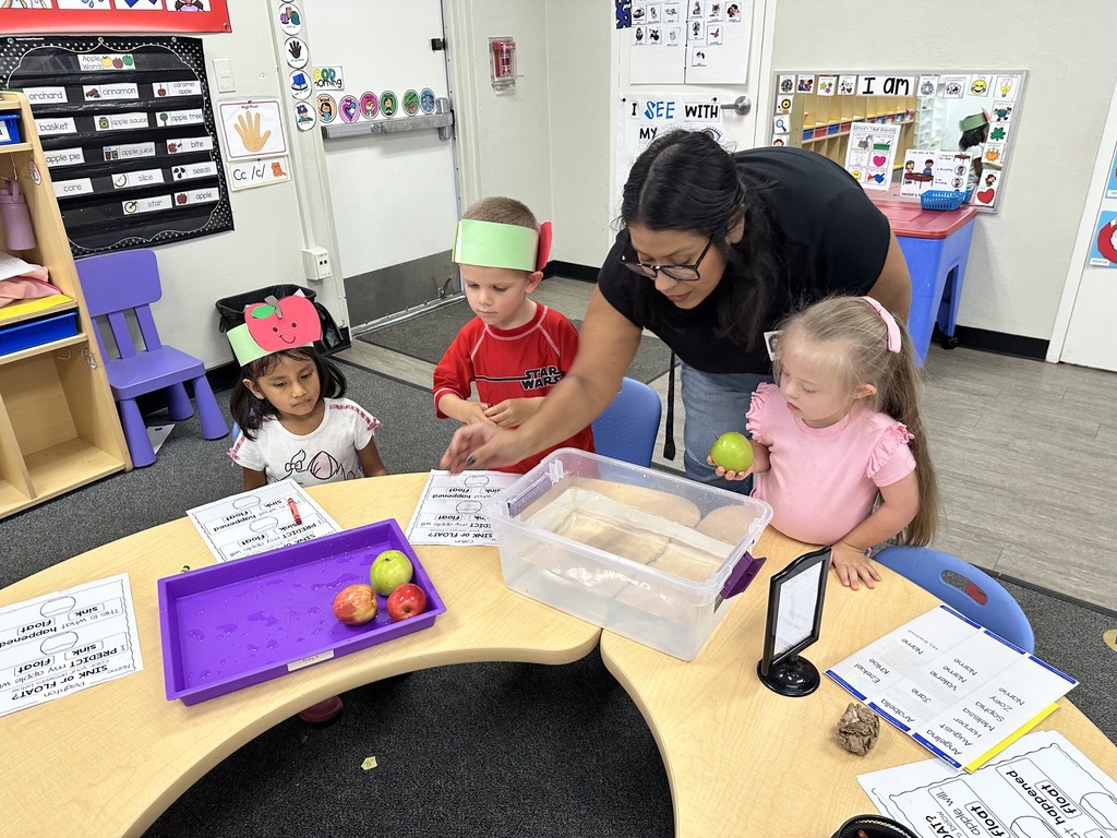 Children wearing apple crowns participate in an apple-themed classroom activity involving apple slices, worksheets.