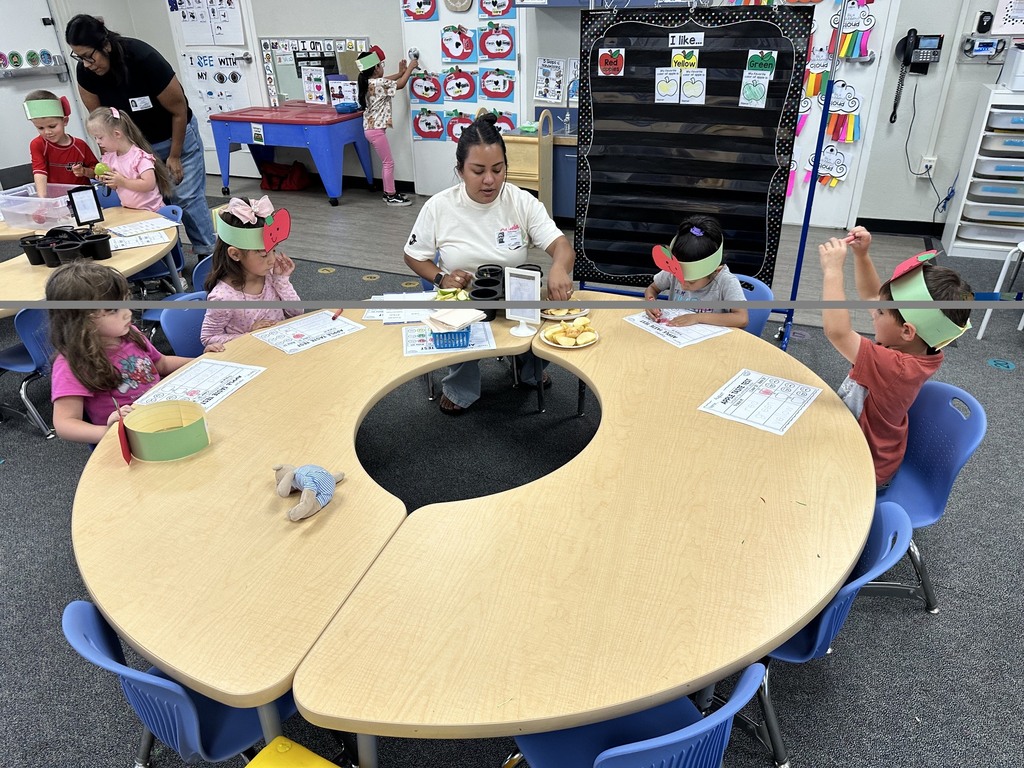 Children wearing apple crowns participate in an apple-themed classroom activity involving apple slices, worksheets.