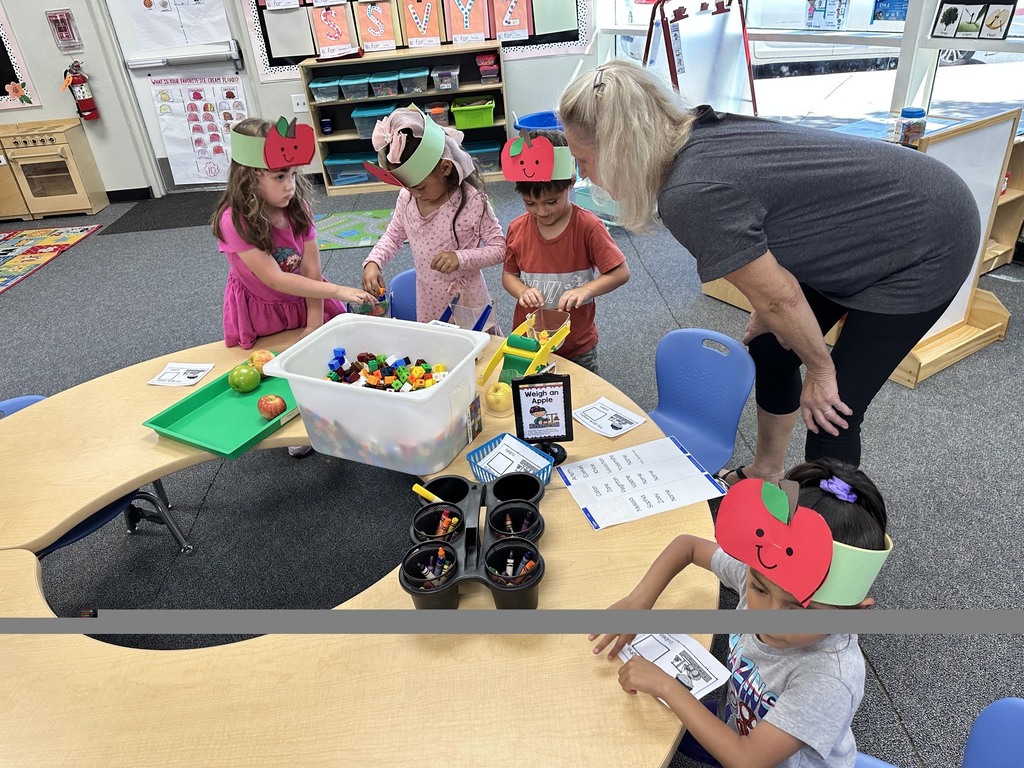 Children wearing apple crowns participate in an apple-themed classroom activity involving apple slices, worksheets.