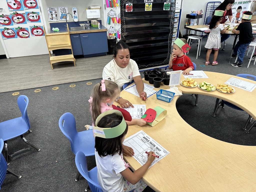 Children wearing apple crowns participate in an apple-themed classroom activity involving apple slices, worksheets.