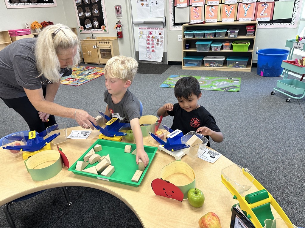 Children wearing apple crowns participate in an apple-themed classroom activity involving apple slices, worksheets.
