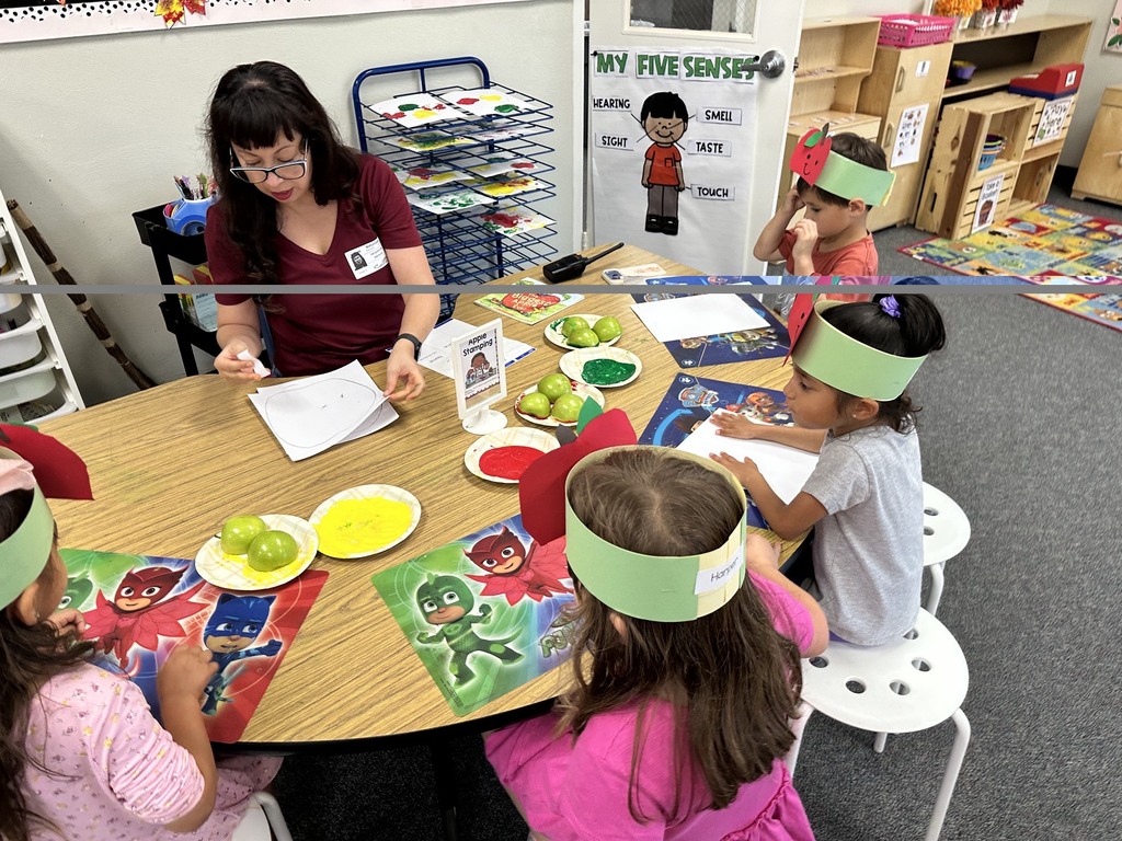Children wearing apple crowns participate in an apple-themed classroom activity involving apple slices, worksheets.