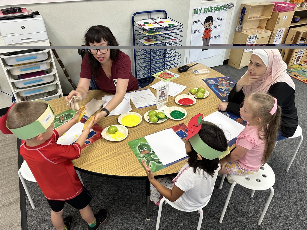 Children wearing apple crowns participate in an apple-themed classroom activity involving apple slices, worksheets.