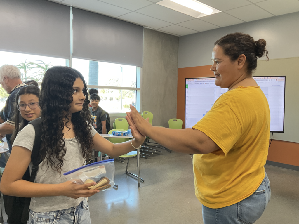 Student high fiving our counselor, Mrs. Fierro, while holding a bag of cookies. 