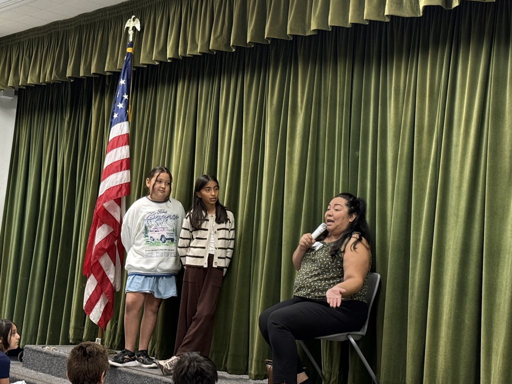 Council woman on the right side wearing green and two students to her right on a stage 