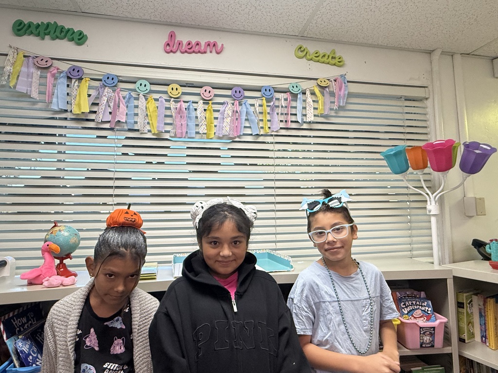 Three students who have crazy hair. The one on the very fat left has a pumpkin on her head, the middle one has ghosts on her pig tails and the one on the right has blue glasses and a grey shirt 