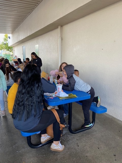 A family enjoying their lunch outdoors while sitting on blue lunch tables