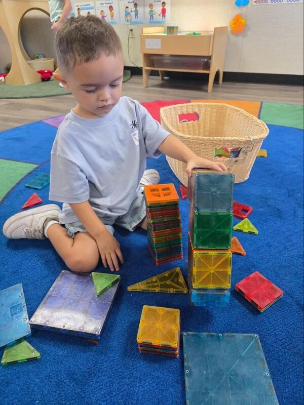 A preschool student builds with magnetic tiles.
