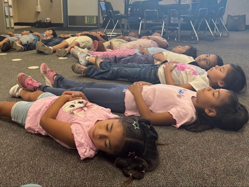 Kindergarten students lay on the floor and practice "otter" breathing.