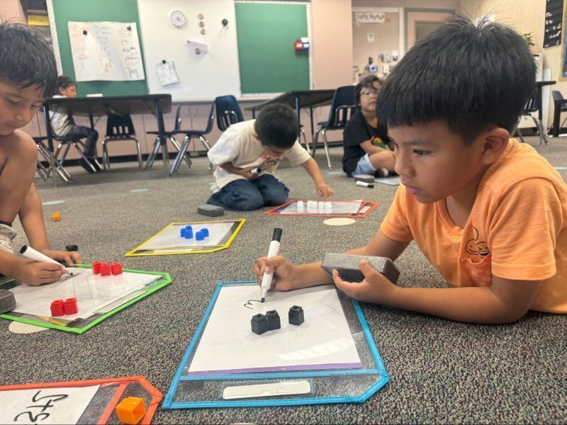 Kindergarten students work on math projects on the floor.