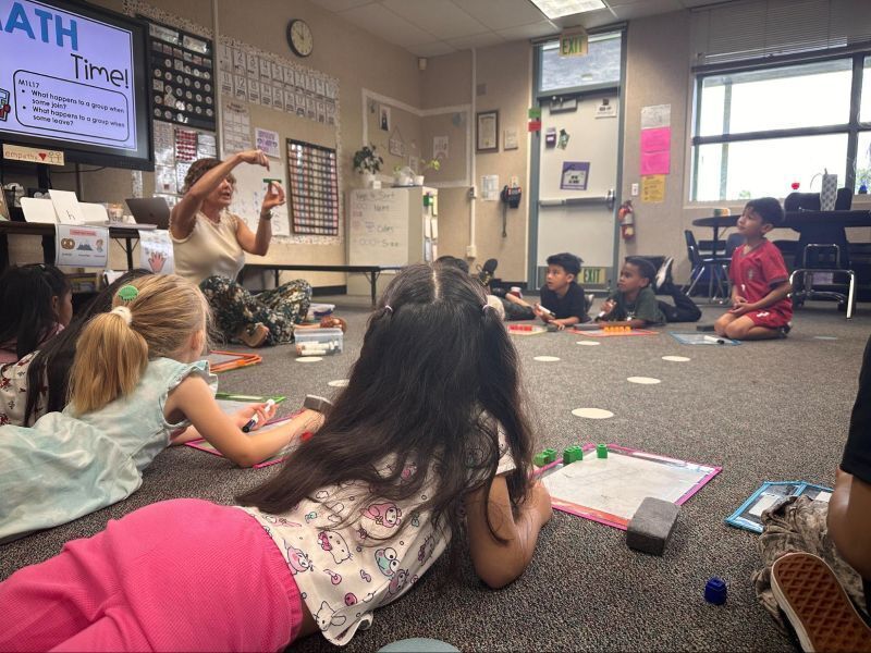 Kindergarten students lay on the floor in a circle as their teacher presents a lesson.