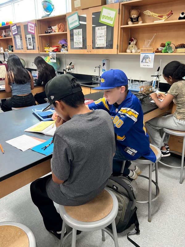 Two students work on a school project. Dos estudiantes trabajan en un proyecto escolar.
