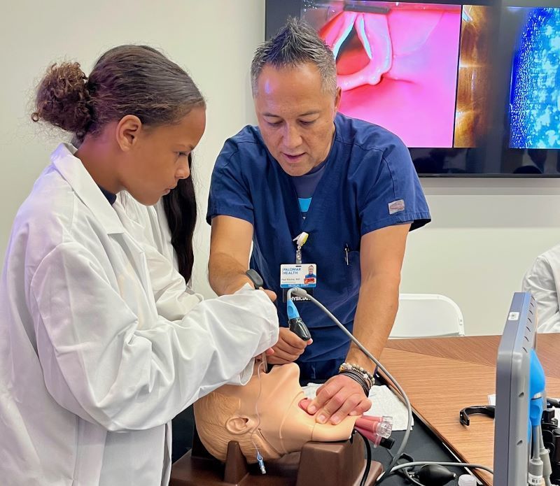 A student practices a medical procedure on a dummy.  Un estudiante practica un procedimiento médico en un maniquí.