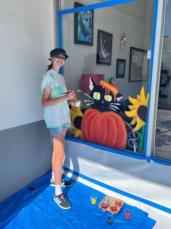 A student poses in front of her window painting.  Una estudiante posa delante de su pintura de ventana.