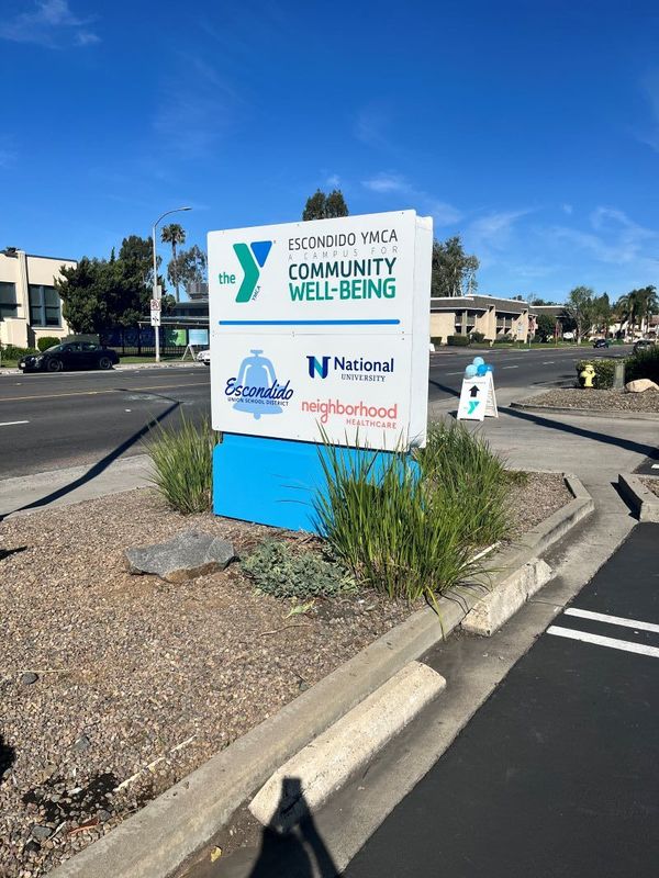 An entry sign depicting, "The Escondido YMCA Community Well-Being, Escondido Union School District, National University, and Neighborhood Healthcare.