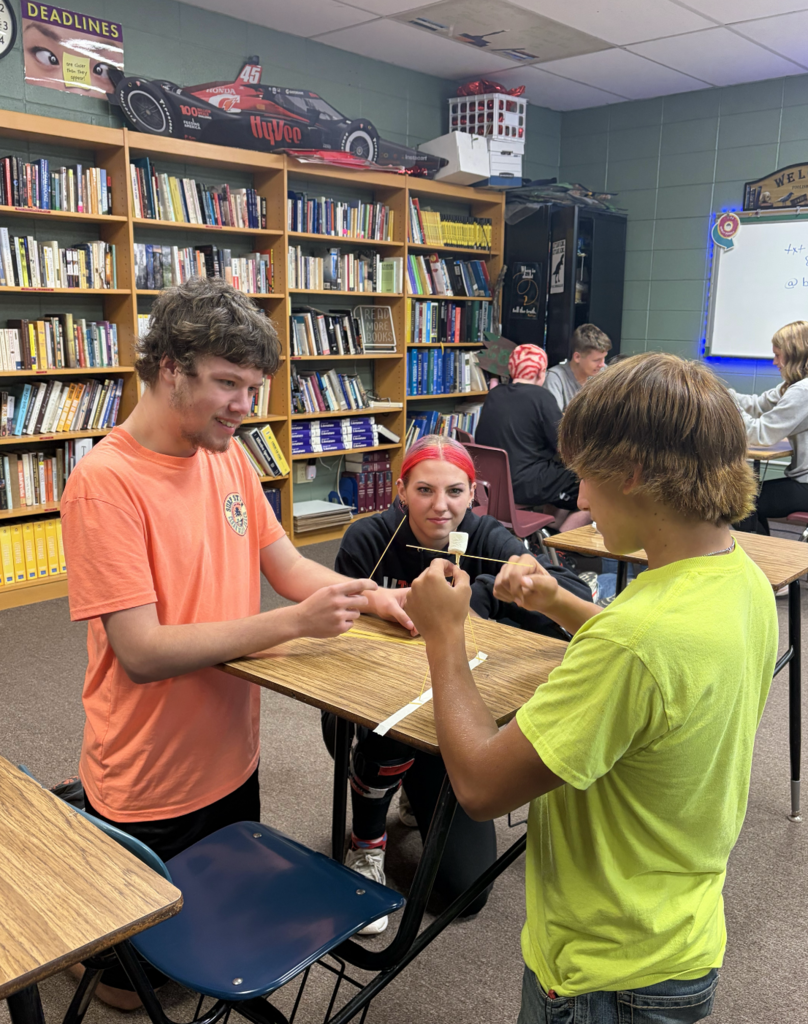 Three students doing a team building exercise around a desk