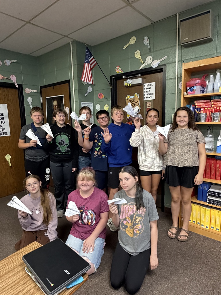 Group of students in a classroom holding paper airplanes