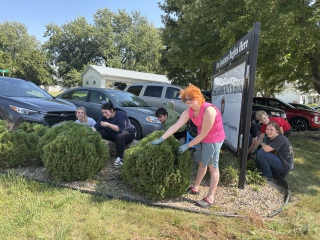 Group of students cleaning the bushes around school sign