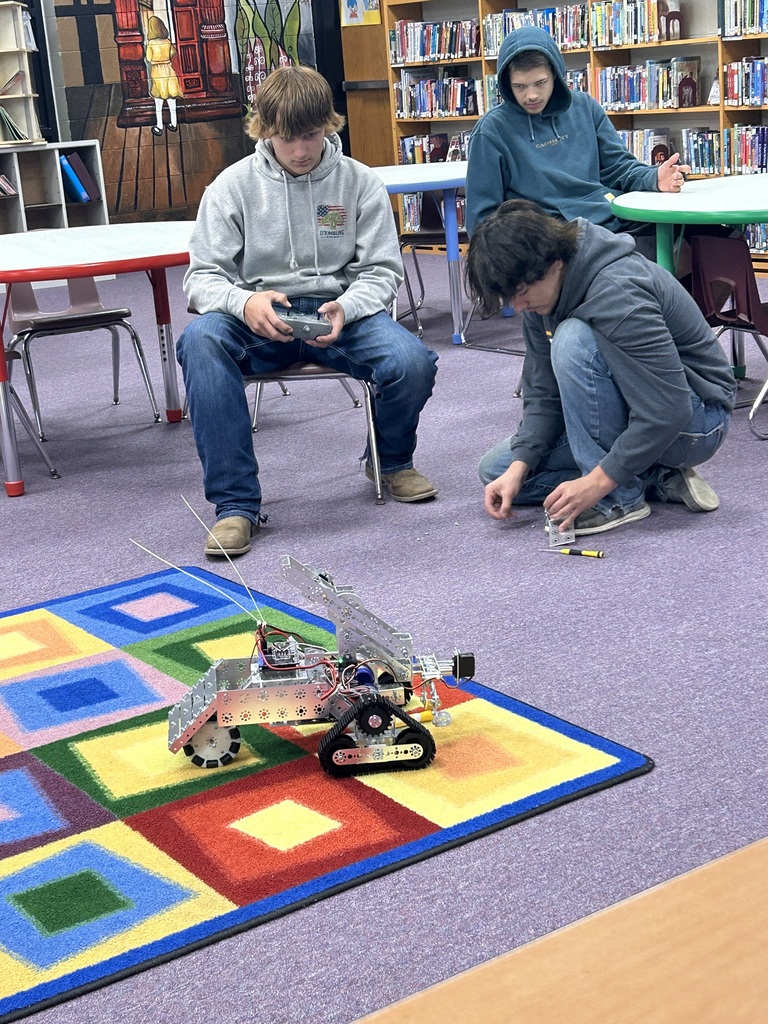Students using remote to drive robot around a library
