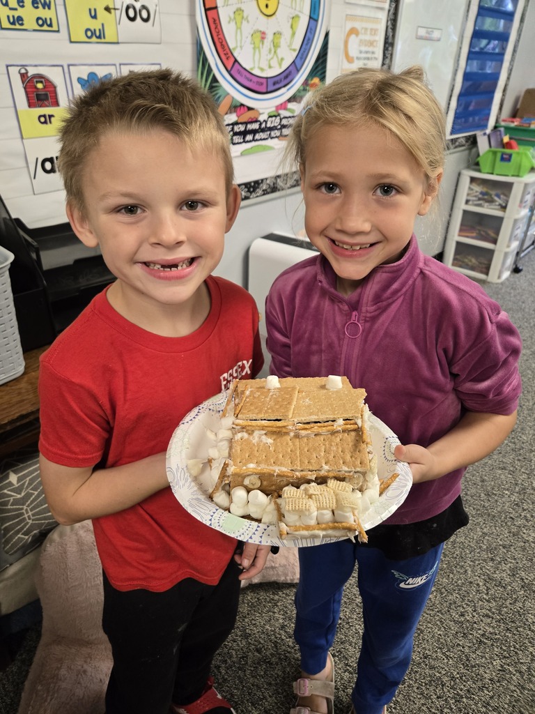 Two students smiling with a candy house they made