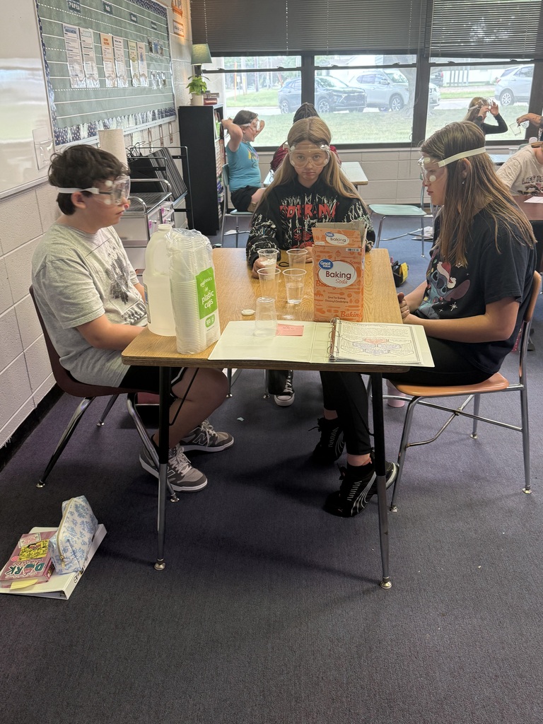 Students sitting around a table with cups of different substances for experiment